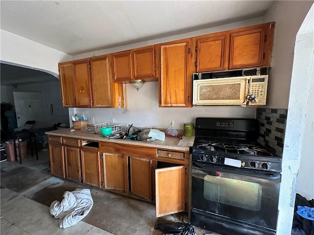 kitchen featuring gas stove, white microwave, brown cabinetry, and light countertops