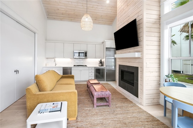 living room with high vaulted ceiling, wood ceiling, sink, light hardwood / wood-style floors, and beverage cooler