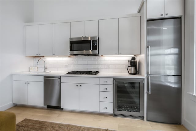 kitchen featuring stainless steel appliances, wine cooler, decorative backsplash, sink, and white cabinets