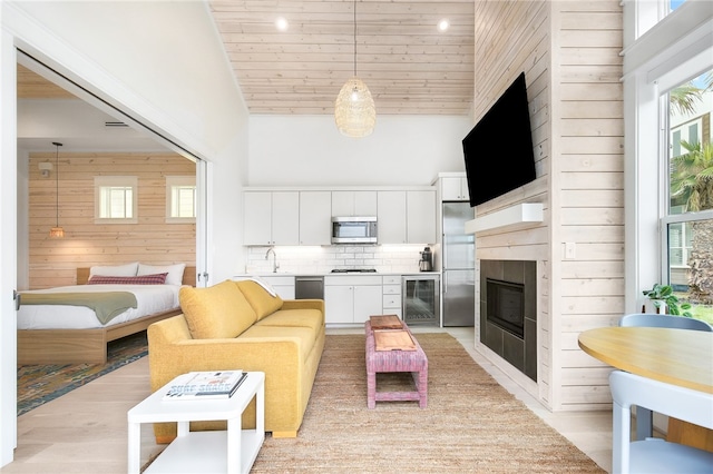 living room with a tiled fireplace, light hardwood / wood-style floors, beverage cooler, sink, and high vaulted ceiling