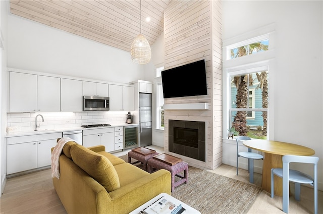 living room with light hardwood / wood-style flooring, wooden ceiling, high vaulted ceiling, a large fireplace, and wine cooler