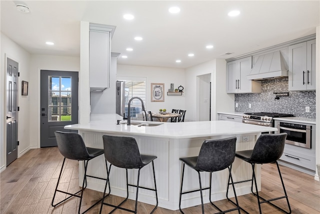 kitchen with custom exhaust hood, light wood finished floors, a sink, a peninsula, and a kitchen bar