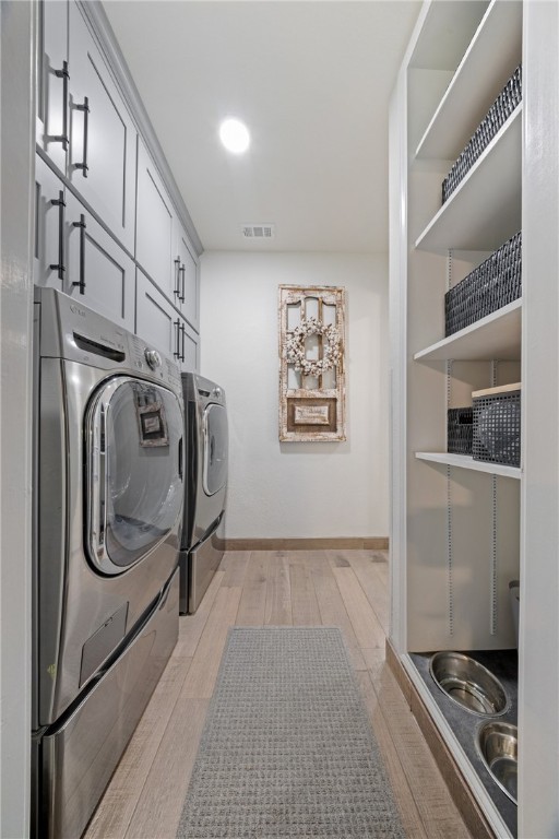 laundry room featuring separate washer and dryer, visible vents, baseboards, cabinet space, and light wood finished floors