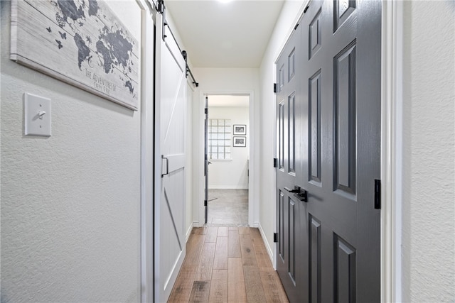 hall with a textured wall, a barn door, wood finished floors, and baseboards