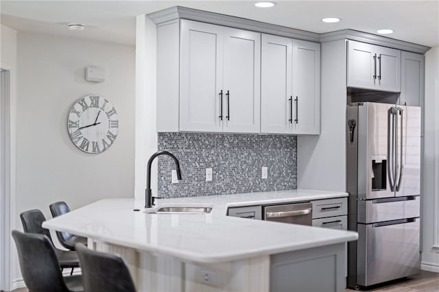 kitchen featuring light countertops, gray cabinetry, appliances with stainless steel finishes, a sink, and a peninsula