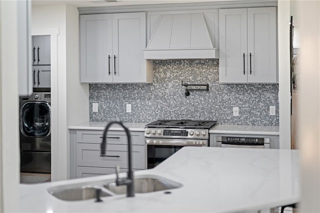 kitchen featuring a sink, stainless steel range with gas cooktop, gray cabinets, custom exhaust hood, and washer / dryer