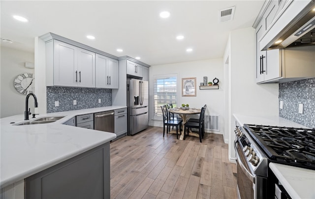 kitchen with visible vents, appliances with stainless steel finishes, a sink, light wood-type flooring, and under cabinet range hood