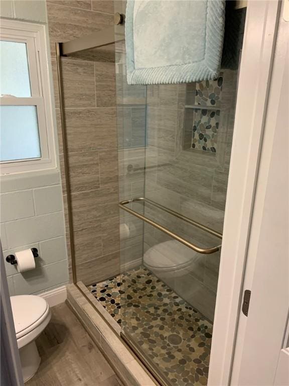 bathroom with toilet, tile walls, wood finished floors, and a stall shower
