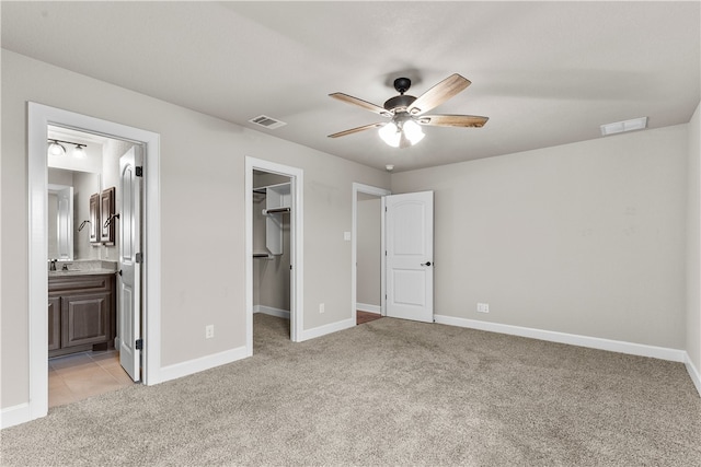 unfurnished bedroom with light carpet, ensuite bathroom, ceiling fan, a walk in closet, and a closet