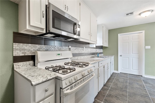 kitchen with sink, white gas range oven, light stone counters, white cabinets, and decorative backsplash