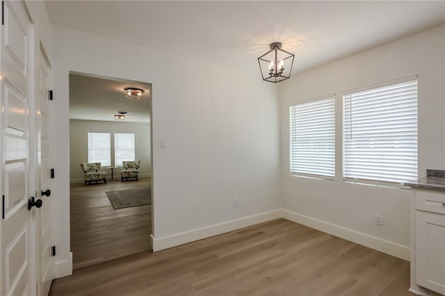 unfurnished dining area with baseboards, light wood-style flooring, and a chandelier