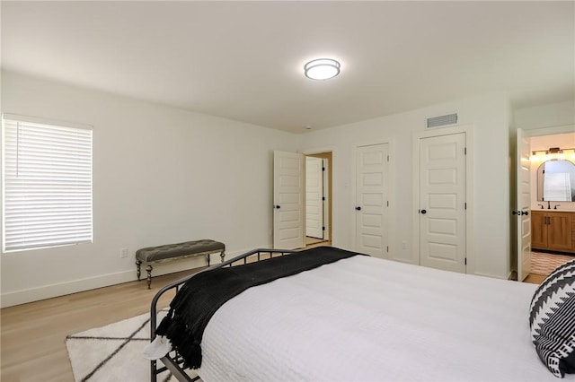 bedroom featuring visible vents, a sink, light wood finished floors, and multiple windows