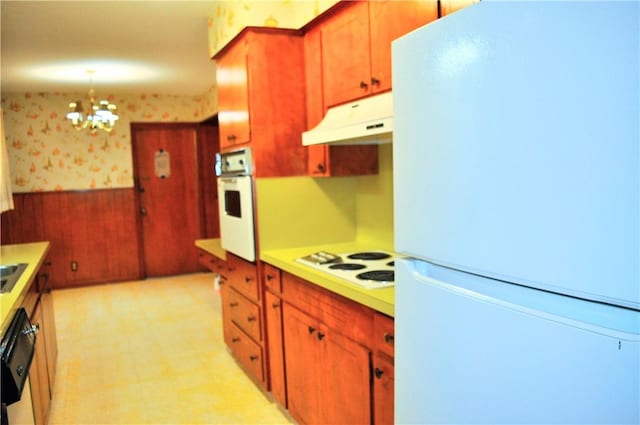 kitchen featuring white appliances, under cabinet range hood, wainscoting, wallpapered walls, and light countertops