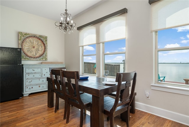 dining space featuring hardwood / wood-style floors, a water view, and a notable chandelier