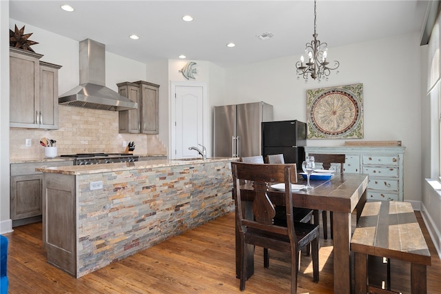 kitchen with wall chimney range hood, black refrigerator, light stone countertops, hardwood / wood-style flooring, and high end fridge