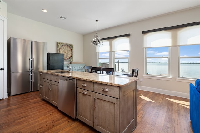 kitchen with light stone countertops, stainless steel appliances, an island with sink, and dark hardwood / wood-style flooring