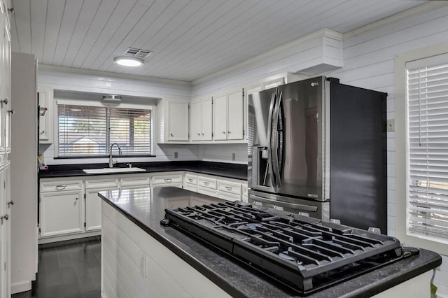 kitchen featuring white cabinetry, sink, black gas cooktop, stainless steel refrigerator with ice dispenser, and wood walls