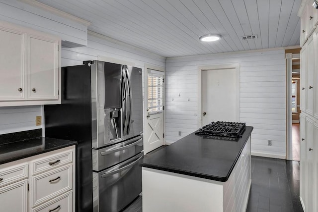 kitchen with stainless steel refrigerator with ice dispenser, white cabinetry, and wooden walls