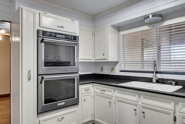 kitchen featuring double oven, white cabinetry, sink, and wooden walls