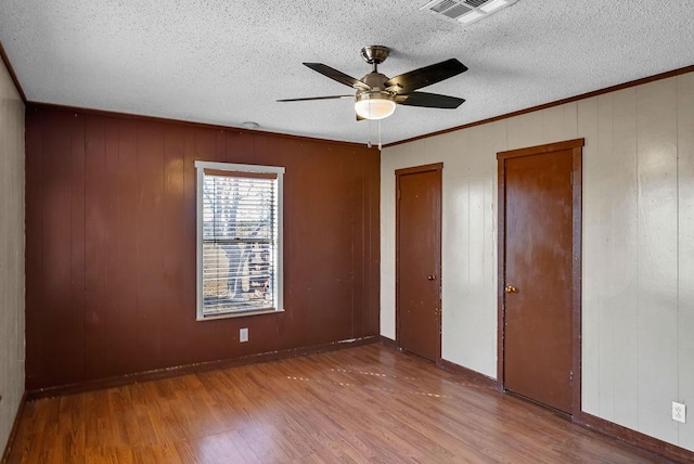 unfurnished bedroom featuring ornamental molding, a textured ceiling, ceiling fan, wooden walls, and hardwood / wood-style flooring