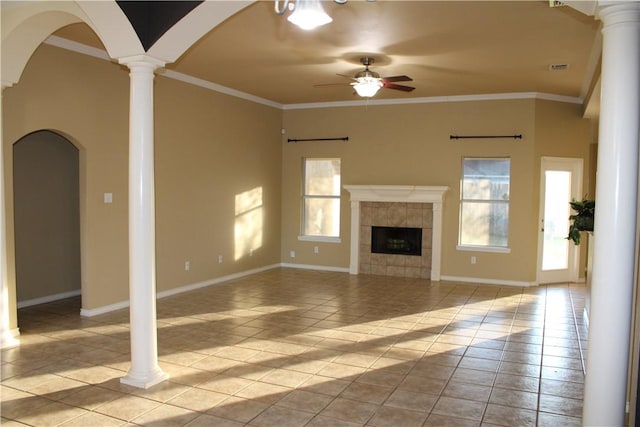 unfurnished living room with ornate columns, ceiling fan, a tile fireplace, crown molding, and light tile patterned floors