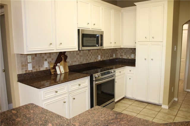 kitchen with white cabinetry, stainless steel appliances, tasteful backsplash, dark stone countertops, and light tile patterned flooring