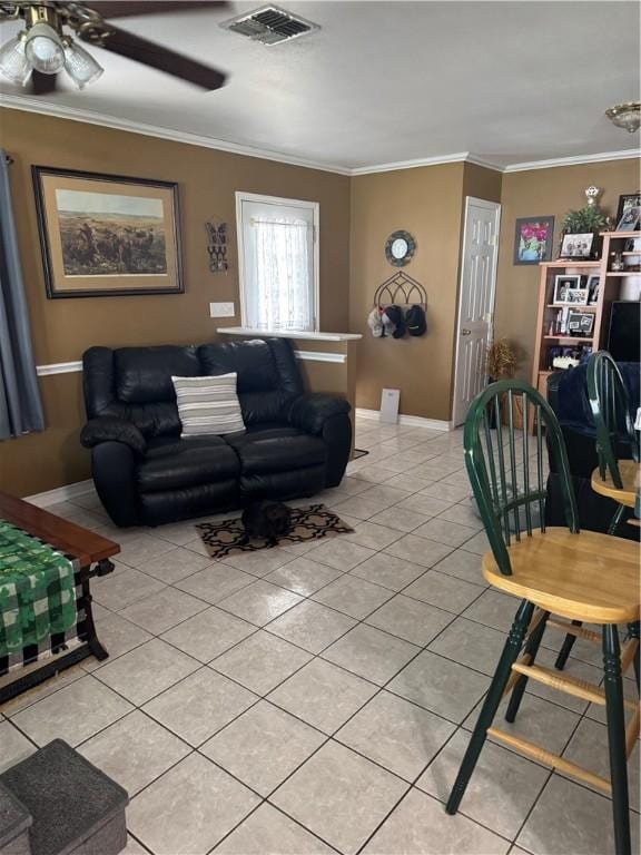 living area with light tile patterned floors, a ceiling fan, baseboards, visible vents, and ornamental molding