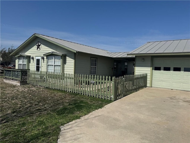 ranch-style house featuring a fenced front yard, metal roof, a garage, driveway, and a standing seam roof