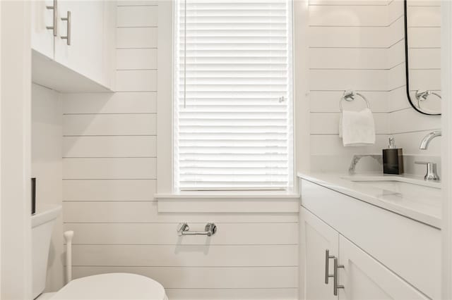 half bath featuring vanity, toilet, and wooden walls