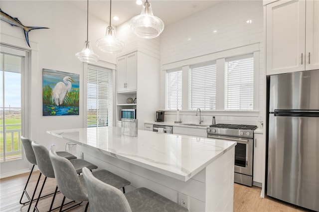 kitchen with appliances with stainless steel finishes, white cabinetry, a sink, a kitchen island, and light wood-type flooring