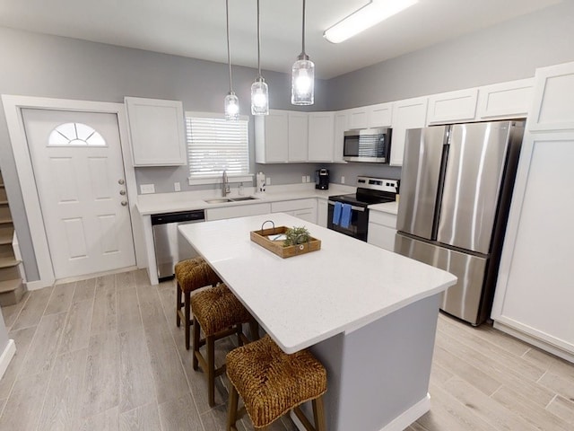 kitchen with stainless steel appliances, a kitchen island, white cabinetry, sink, and light hardwood / wood-style flooring