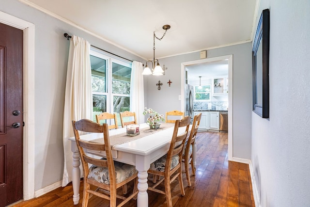 dining area with dark wood-type flooring, an inviting chandelier, and ornamental molding