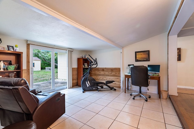 office area with a textured ceiling, lofted ceiling, wooden walls, and light tile patterned floors