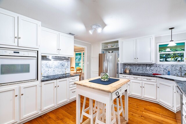 kitchen featuring stainless steel refrigerator, sink, decorative light fixtures, white oven, and light wood-type flooring