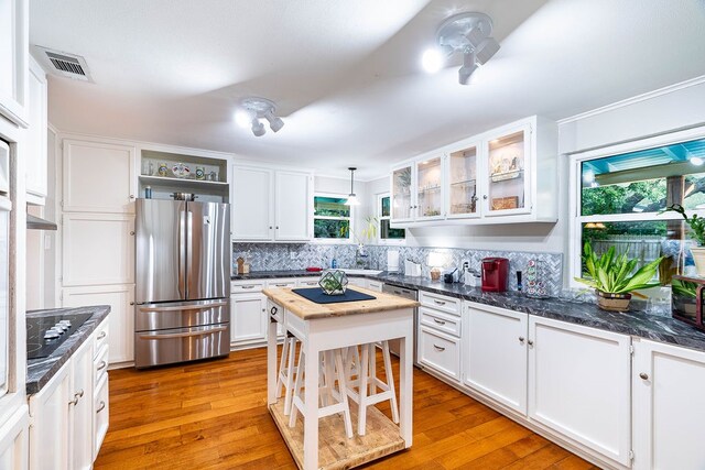 kitchen with hanging light fixtures, stainless steel fridge, a healthy amount of sunlight, and white cabinetry