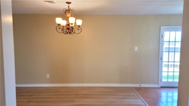 unfurnished room featuring an inviting chandelier and hardwood / wood-style flooring