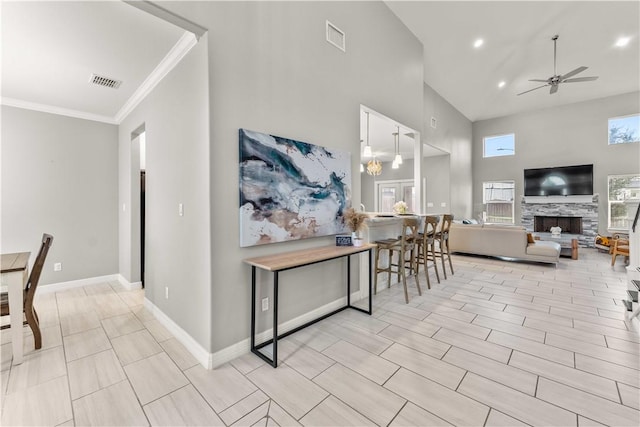 dining area featuring ceiling fan, a high ceiling, a stone fireplace, and ornamental molding