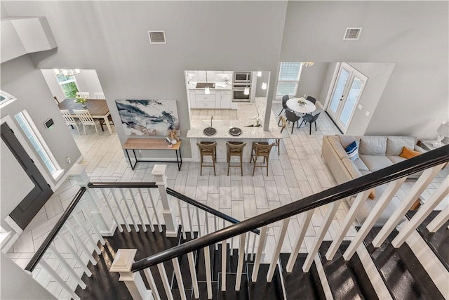 stairs with hardwood / wood-style floors, a towering ceiling, a notable chandelier, and french doors