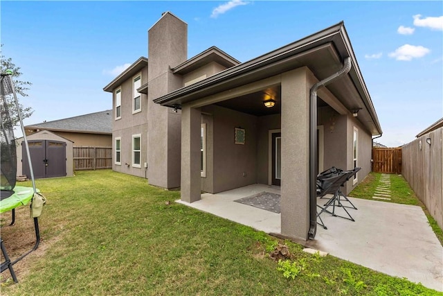 rear view of property with a lawn, a patio, a storage shed, and a trampoline