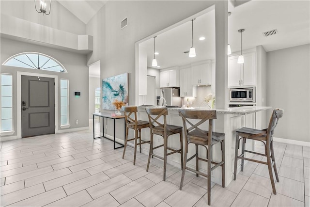 kitchen with pendant lighting, appliances with stainless steel finishes, white cabinets, light stone countertops, and high vaulted ceiling