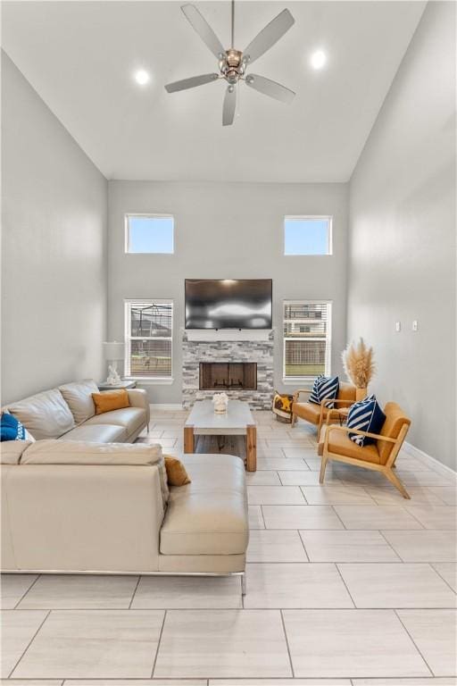 living room featuring ceiling fan, a towering ceiling, and a stone fireplace