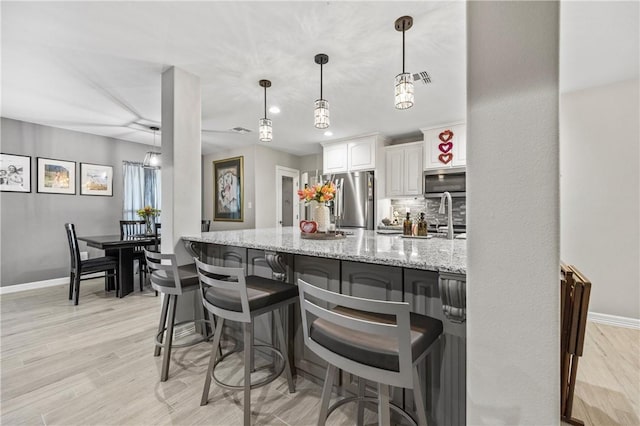 kitchen with white cabinetry, a kitchen breakfast bar, light stone counters, stainless steel appliances, and light hardwood / wood-style flooring