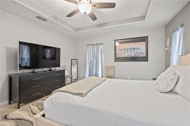 bedroom with a tray ceiling, light hardwood / wood-style floors, and ceiling fan