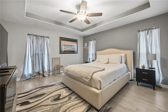 bedroom featuring a raised ceiling, ceiling fan, and light hardwood / wood-style floors