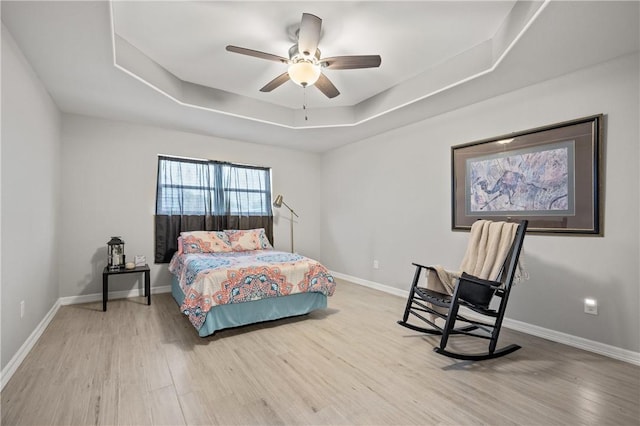 bedroom featuring ceiling fan, a tray ceiling, and light wood-type flooring