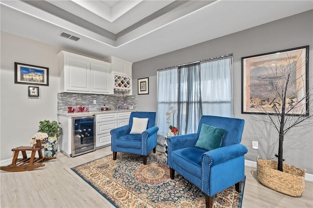 living area featuring bar, beverage cooler, a tray ceiling, and light wood-type flooring