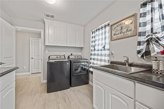 laundry room with sink, washing machine and dryer, cabinets, and light wood-type flooring