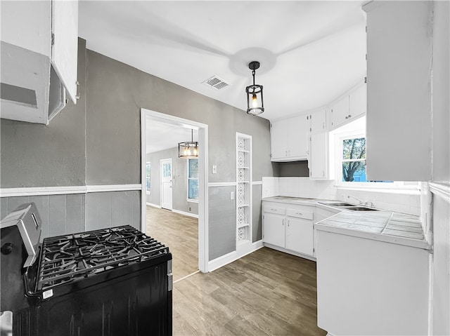 kitchen with pendant lighting, light hardwood / wood-style flooring, white cabinetry, tile counters, and stainless steel range with gas stovetop