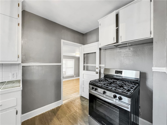 kitchen with decorative backsplash, white cabinetry, dark wood-type flooring, and stainless steel gas range