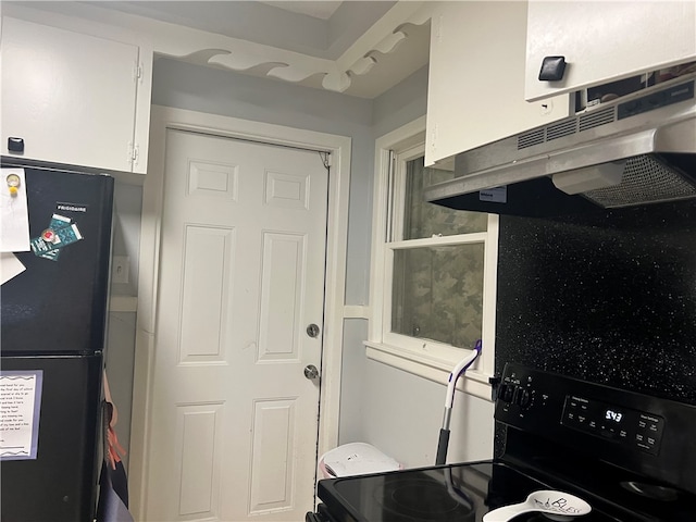 kitchen with white cabinetry, black fridge, backsplash, range hood, and stove